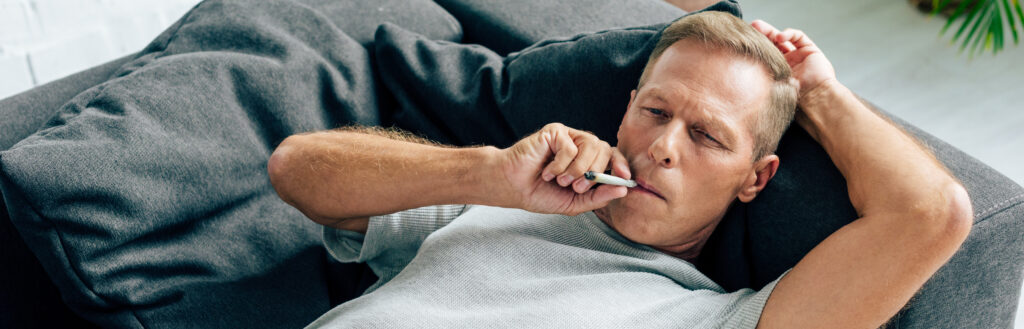 An older man is smoking weed while on the couch; he needs treatment here at The Encino Detox.